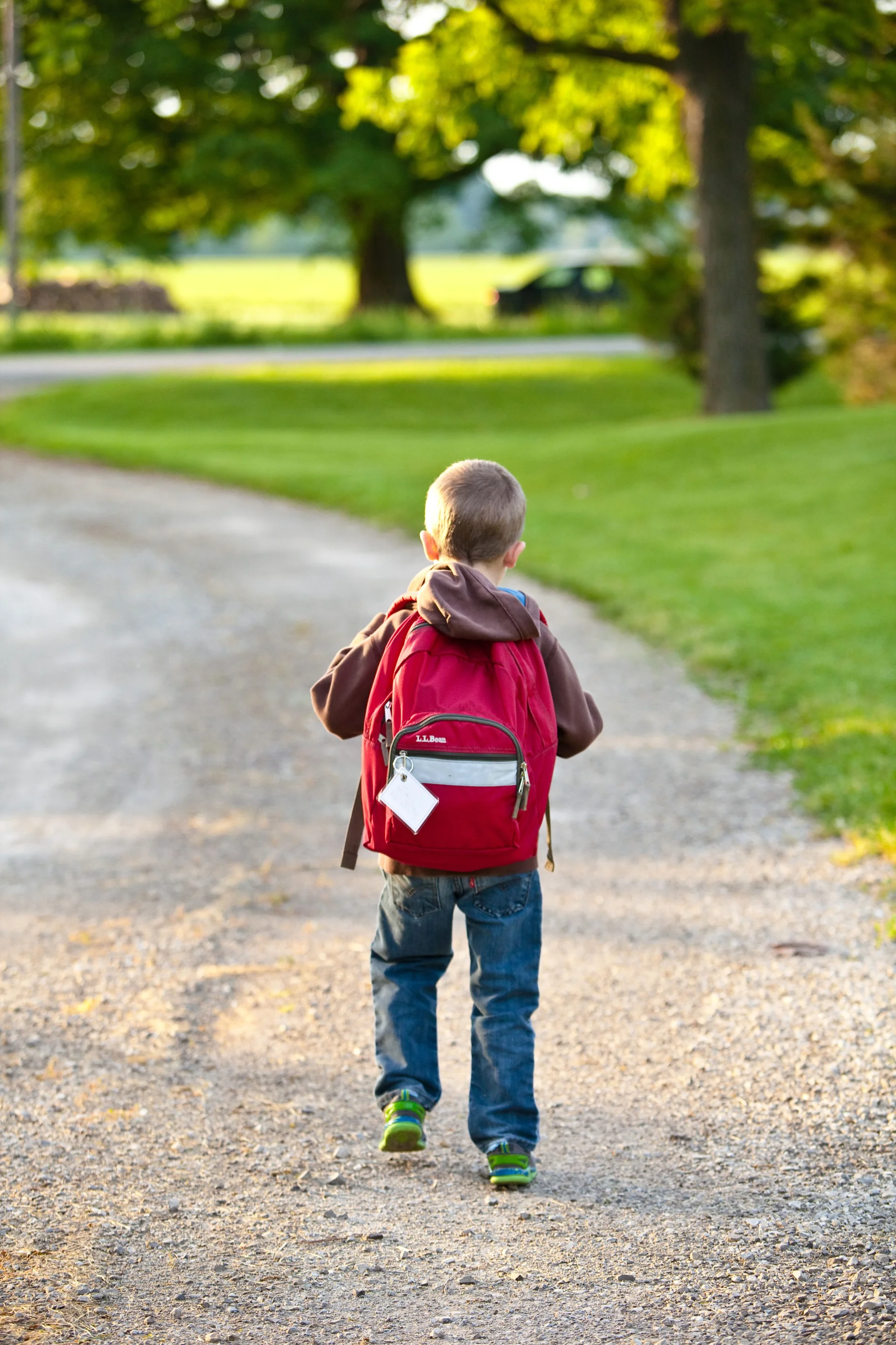 Young child wearing a red L.L.Bean backpack walking down a gravel path on the first day of school